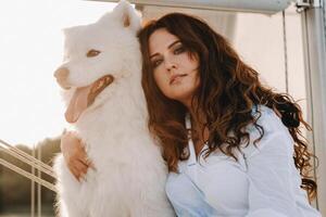 uma feliz mulher com uma grande branco cachorro em uma branco iate dentro a mar foto