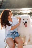 uma feliz mulher com uma grande branco cachorro em uma branco iate dentro a mar foto