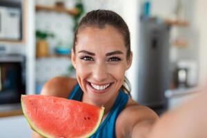 jovem mulher come uma fatia do Melancia dentro a cozinha. retrato do jovem mulher desfrutando uma Melancia. foto