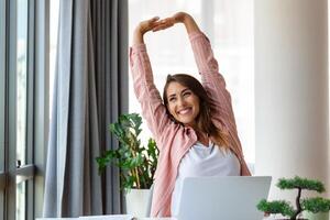 jovem mulher trabalhando em computador portátil. o negócio mulher ocupado trabalhando em computador portátil alongamento. empresária sentado às brilhante moderno trabalhos estação foto