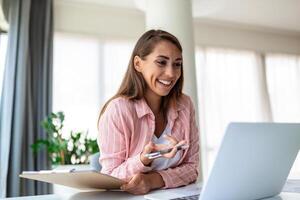 trabalho remoto, tecnologia e conceito de pessoas - mulher de negócios jovem sorridente feliz com computador portátil e papéis trabalhando no escritório em casa foto