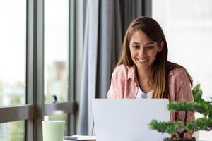 jovem o negócio mulher usando computador portátil às lar, olhando às tela, conversando, lendo ou escrevendo e-mail, sentado em sofá, fêmea aluna fazendo trabalho de casa, trabalhando em pesquisa projeto conectados foto