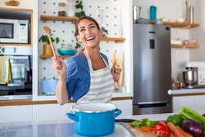 engraçado lindo mulher cantando para dentro espátula, cozinhando dentro moderno cozinha, segurando espátula Como microfone, dançando, ouvindo para música, brincalhão menina tendo Diversão com utensílios de cozinha, preparando Comida. foto