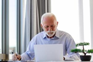 financeiro orientador homem de negocios usando dele computador portátil e fazendo alguns papelada enquanto sentado às escrivaninha e trabalhando. foto