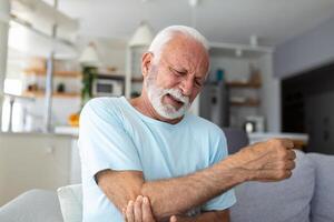 Senior homem com braço dor.velho masculino massageando doloroso mão dentro de casa. velho homem mão segurando dele cotovelo sofrimento a partir de cotovelo dor. Senior homem sofrimento a partir de dor dentro mão às lar. velho idade, saúde foto