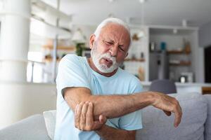 Senior homem com braço dor.velho masculino massageando doloroso mão dentro de casa. velho homem mão segurando dele cotovelo sofrimento a partir de cotovelo dor. Senior homem sofrimento a partir de dor dentro mão às lar. velho idade, saúde foto