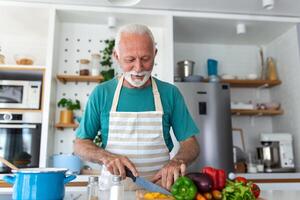 feliz aposentado Senior homem cozinhando dentro cozinha. aposentadoria, passatempo pessoas conceito. retrato do sorridente Senior homem corte legumes foto