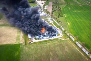 aéreo Visão do queimado industrial armazém ou logística Centro construção depois de grande fogo com enorme fumaça a partir de queimado cobertura foto