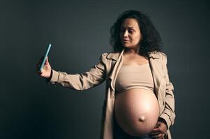 feliz jovem grávida mulher, expectante mãe fotografando dela lindo grande barriga dentro último trimestre do feliz gravidez foto