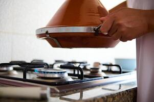 fechar-se dona de casa segurando uma argila Panela tagine acima a forno, cozinhando delicioso refeição dentro a casa cozinha foto