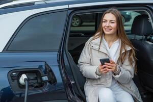 jovem mulher cobrando dela elétrico carro às uma cobrando estação dentro a cidade. eco combustível conceito. a conceito do ambientalmente amigáveis transporte. recarregar bateria a partir de cobrando estação. foto