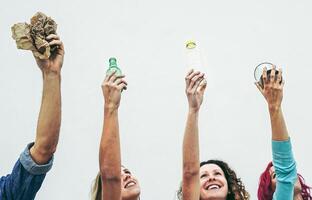 feliz pessoas segurando reciclável objetos Como papel, vidro, plástico, alumínio em uma branco fundo - eco conceito com reciclando - foco em mãos foto