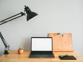 laptop e algumas ferramentas fixas na mesa de trabalho de madeira com uma parede cinza vazia como pano de fundo. conceito de espaço de trabalho e escritório mínimo. foto