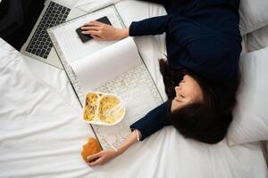 ocupado e cansado empresária comendo pão para café da manhã dentro cama às casa e trabalhando para entregar financeiro afirmações para uma chefe. sobrecarregado e pouco saudável para pronto refeições, esgotamento conceito. foto