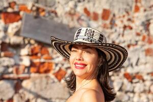 lindo mulher vestindo a tradicional colombiano chapéu chamado sombrero vueltiao às san ignácio baluarte dentro a histórico cartagena de índias murado cidade foto