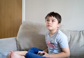 retrato criança jogando vídeo jogo. criança segurando console jogar jogos conectados com amigos às lar, jovem Garoto localização sofá tendo Diversão e relaxante em dele próprio em final de semana foto