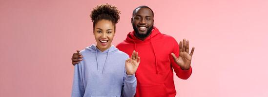 feliz afro-americano casal homem mulher abraçando amigáveis cara abraçando menina solidário juntos acenando você cumprimento dizer Olá sorridente alegremente convidativo venha dentro acolhedor, em pé Rosa fundo foto