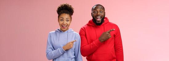 impressionado dois melhor amigos africano americano homem mulher 25s solta mandíbula divertido Visita impressionante interessante parque apontando esquerda índice dedos ampliar olhos emocionados tendo Diversão junto, em pé Rosa fundo foto