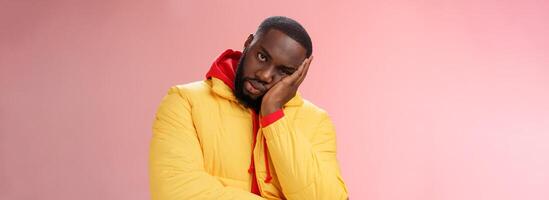 irritado incomodado chateado afro-americano barbudo homem dentro amarelo Jaqueta facepalm Veja Bravo Câmera irritado magro cabeça mão entediado alimentado acima chateado audição desinteressante mesmo histórias, Rosa fundo foto