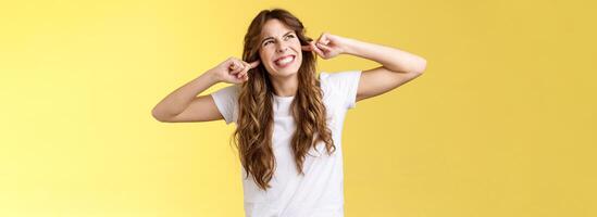 Bravo descontente irritado cabelo encaracolado lindo menina fazendo careta faço irônico face olhar fixamente acima irritado ruído chegando a partir de vizinhos acima apertar dentes plugue índice dedos orelhas ódio alto música jogando foto