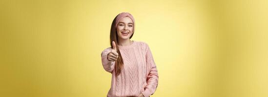 gestos, emoções e estilo de vida conceito. confiante positivo 20s europeu mulher vestindo casual suéter sobre amarelo fundo mostrando polegar acima gesto, aprovando, aceitando e gosto conceito foto