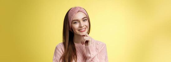 feliz jovem europeu mulher dentro tricotado arco de cabelo, suéter inclinação cabeça tocante queixo e sorridente bobagem, levando Cuidado do pele, sentindo-me face cintilante olhando Claro e saudável depois de cuidados com a pele tratamento foto