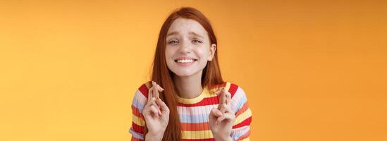 atraente ruiva esperançoso menina antecipando Boa notícia excitação emoção Cruz dedos Boa sorte sorridente amplamente Rezar desejo venha verdade Boa resultados receber prêmio, em pé laranja fundo desejo foto