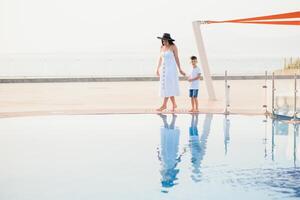 fofa feliz família tendo Diversão perto piscina em luxo tropical recorrer, mãe com criança, verão feriados, amor conceito foto