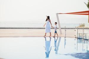 fofa feliz família tendo Diversão perto piscina em luxo tropical recorrer, mãe com criança, verão feriados, amor conceito foto