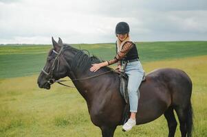 jovem mulher equitação uma cavalo em a verde campo foto