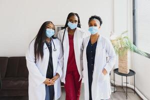 grupo do cuidados de saúde trabalhadores vestindo protetora face máscaras enquanto em pé com braços cruzado e olhando às Câmera foto