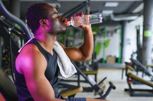 africano americano fisiculturista segurando caneca com água às moderno Academia foto