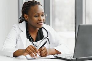 africano americano mulher médico trabalhando às dela escritório conectados usando portátil informação dispositivo. telemedicina Serviços. primário Cuidado consultas, psicoterapia, emergência Serviços foto