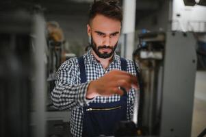 masculino fábrica trabalhador trabalhando ou manutenção com a máquina dentro a industrial fábrica enquanto vestindo segurança uniforme e Difícil chapéu. foto