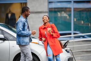 feliz jovem adulto africano americano homem e sorridente mulher cobrando elétrico carro. foto