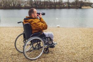 paraplégico deficiente homem dentro cadeira de rodas é fotografando ar livre. foto