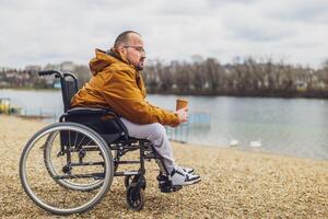 paraplégico deficiente homem dentro cadeira de rodas é desfrutando ao ar livre e bebendo café. foto