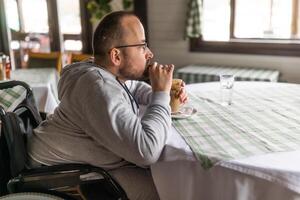 paraplégico deficiente homem dentro cadeira de rodas é sentado às restaurante e bebendo café. foto