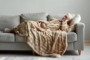 ai gerado doente homem com cobertor deitado em cinzento sofá. generativo ai foto