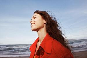 alegre mulher abraçando liberdade em ensolarado praia, vestindo vermelho roupas foto