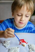 a criança desenha e tintas gesso figuras com uma escova e guache em uma peça do papel. foto