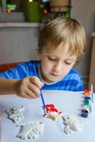 a criança desenha e tintas gesso figuras com uma escova e guache em uma peça do papel. foto