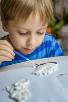 a criança desenha e tintas gesso figuras com uma escova e guache em uma peça do papel. foto