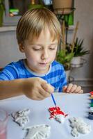 a criança desenha e tintas gesso figuras com uma escova e guache em uma peça do papel. foto