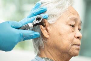 audiologista ou ent médico usar otoscópio verificação orelha do ásia Senior mulher paciente tratando audição perda problema. foto