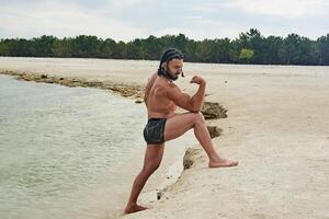 jovem muscular homem exercício em a praia, jovem muscular homem fazendo musculação exercícios em a praia, Atlético jovem homem em a de praia foto