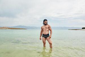 jovem muscular homem exercício em a praia, jovem muscular homem fazendo musculação exercícios em a praia, Atlético jovem homem em a de praia foto