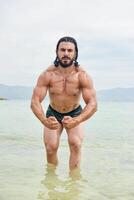 jovem muscular homem exercício em a praia, jovem muscular homem fazendo musculação exercícios em a praia, Atlético jovem homem em a de praia foto