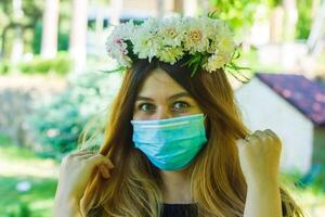 jovem mulher com médico mascarar dentro uma guirlanda do flores foto