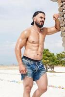 jovem muscular homem exercício em a praia, jovem muscular homem fazendo musculação exercícios em a praia, Atlético jovem homem em a de praia foto